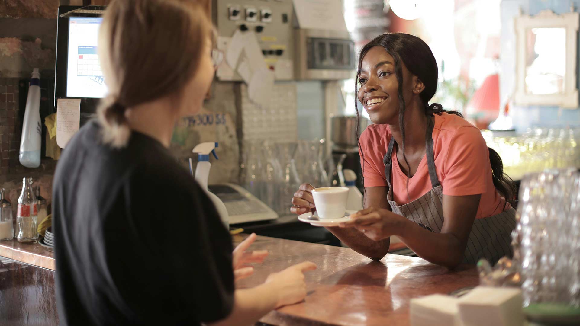 Happy black female barista serving coffee in cup in cafe