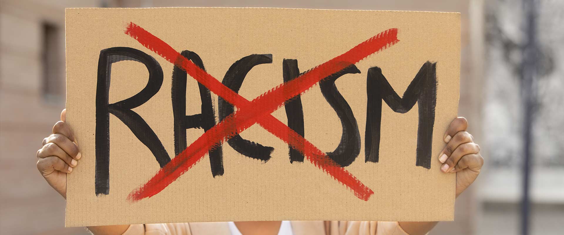 Someone holding up a cardboard sign saying Racism with a red X over it