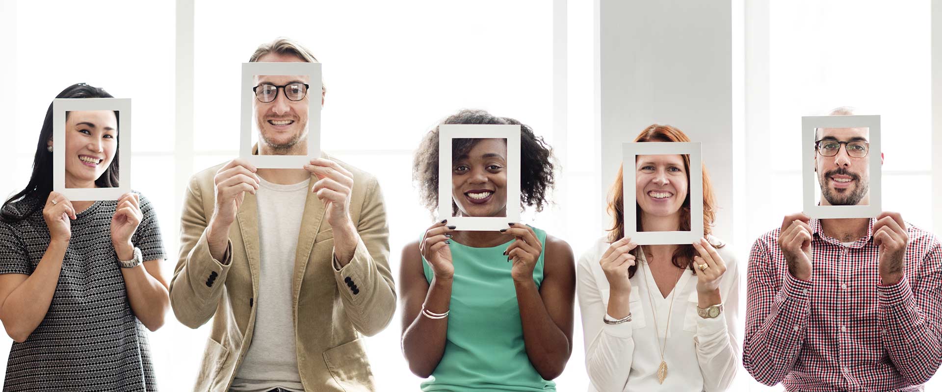 Picture of a diverse group of people holding up an empty picture frame to their faces so you can see their faces behind them
