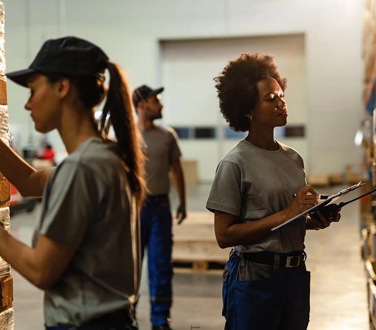 Two women working in a warehouse checking inventory with a man in the background
